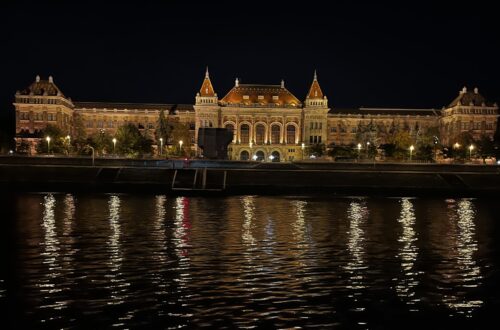 Opplyst historisk bygning langs Donau i Budapest om natten, med gylne lys som speiler seg i elven.