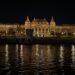Opplyst historisk bygning langs Donau i Budapest om natten, med gylne lys som speiler seg i elven.