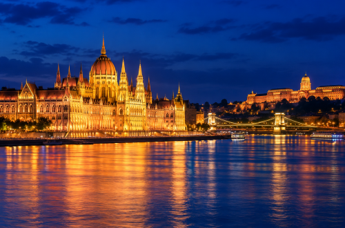 Illuminated historic building along the Danube in Budapest at night, with golden lights reflecting on the river.
